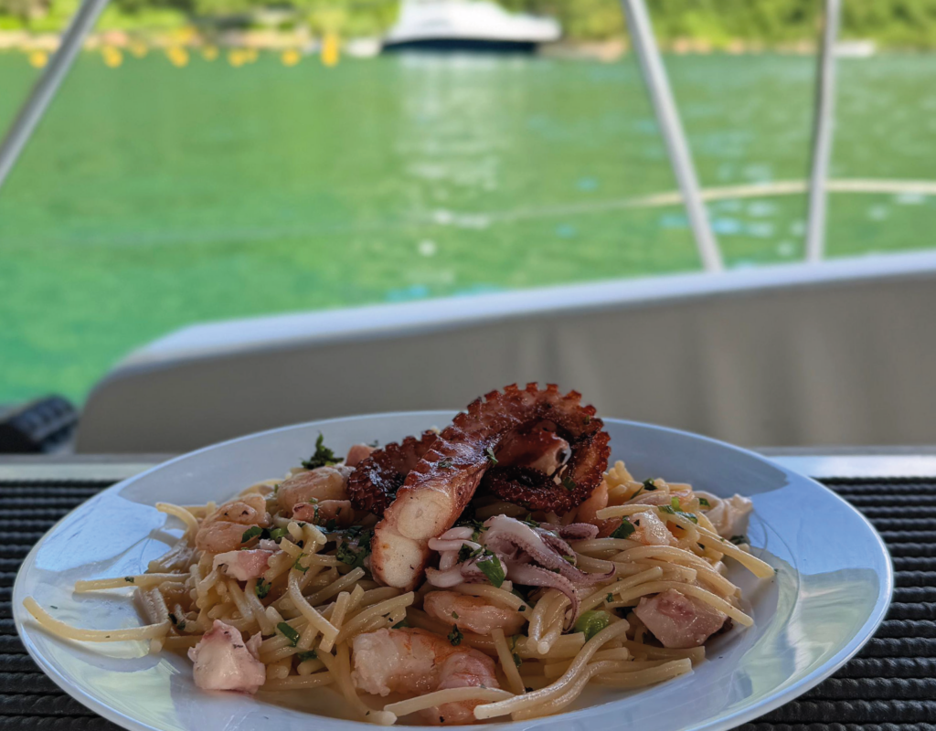 Massa ao alho e óleo com frutos do mar servida em um prato branco em uma mesa abordo de um catamaran