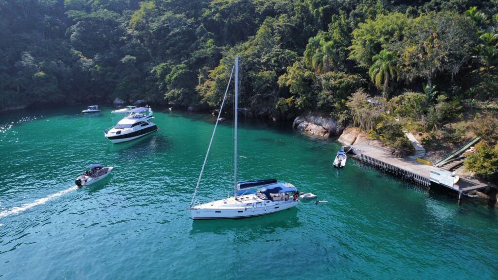 Barcos ancorados em praia reservada de água cristalina e paisagem exuberante, em Paraty, RJ.